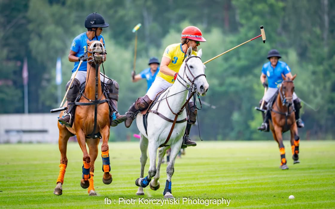 Two riders on horseback contest the ball during a polo match on a grass field.