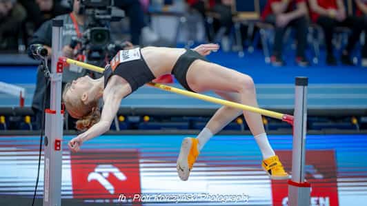 Zawodniczka pokonuje poprzeczkę w skoku wzwyż na hali sportowej.