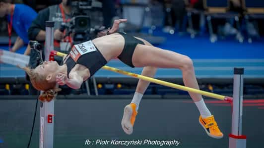 Skoczkini wzwyż pokonuje poprzeczkę tyłem podczas próby na hali lekkoatletycznej.