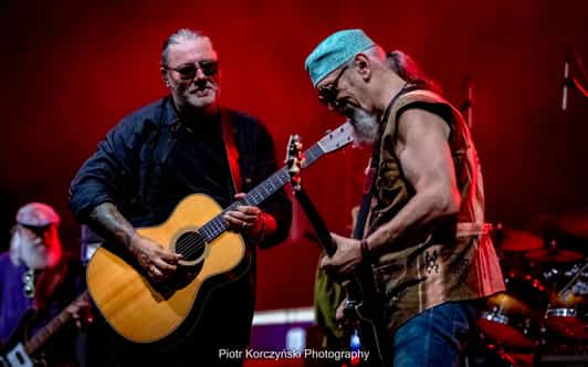 Dwóch muzyków gra na gitarach na scenie skąpanej w czerwonym świetle.
