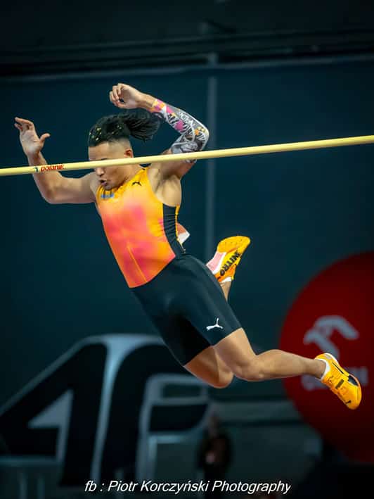 Zawodniczka w stroju lekkoatletycznym pokonuje poprzeczkę podczas skoku wzwyż w hali.