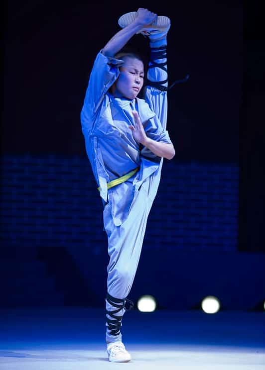 Praktykujący w klasztorze Shaolin wykonuje wysokie pionowe kopnięcie na oświetlonej scenie.