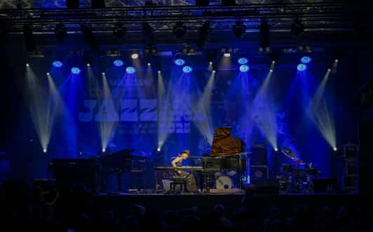 Pianistka gra przy fortepianie na oświetlonej niebieskim światłem scenie z widocznym napisem JAZZ.