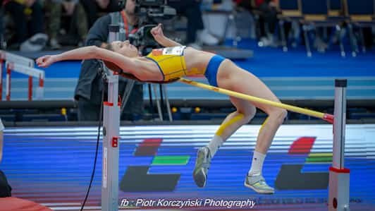 Skoczkini wzwyż przechodzi nad poprzeczką podczas próby na hali lekkoatletycznej.