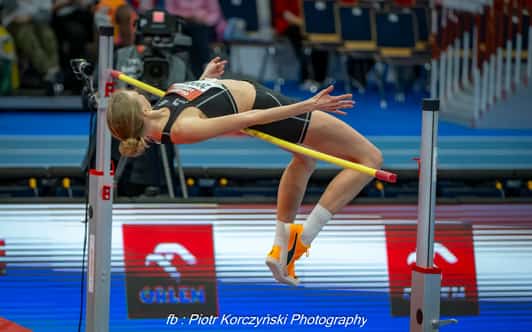 Zawodniczka skacze wzwyż techniką flop nad poprzeczką w hali lekkoatletycznej.