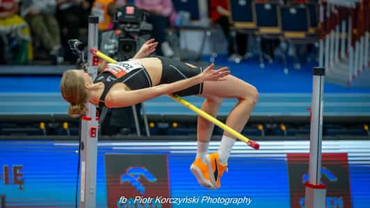 Zawodniczka pokonuje poprzeczkę podczas skoku wzwyż na hali lekkoatletycznej.