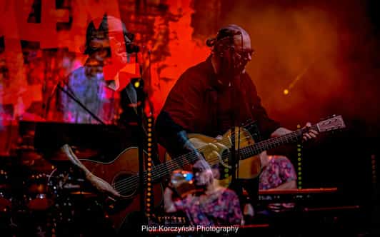 Dwukrotna ekspozycja pokazuje gitarzystę na scenie w czerwonym świetle i dymie podczas koncertu zespołu DŻEM.