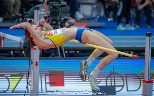 Zawodniczka pokonuje poprzeczkę w skoku wzwyż na hali lekkoatletycznej.