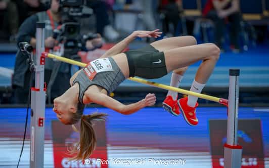 Skoczkini wzwyż pokonuje poprzeczkę tyłem podczas zawodów lekkoatletycznych w hali.